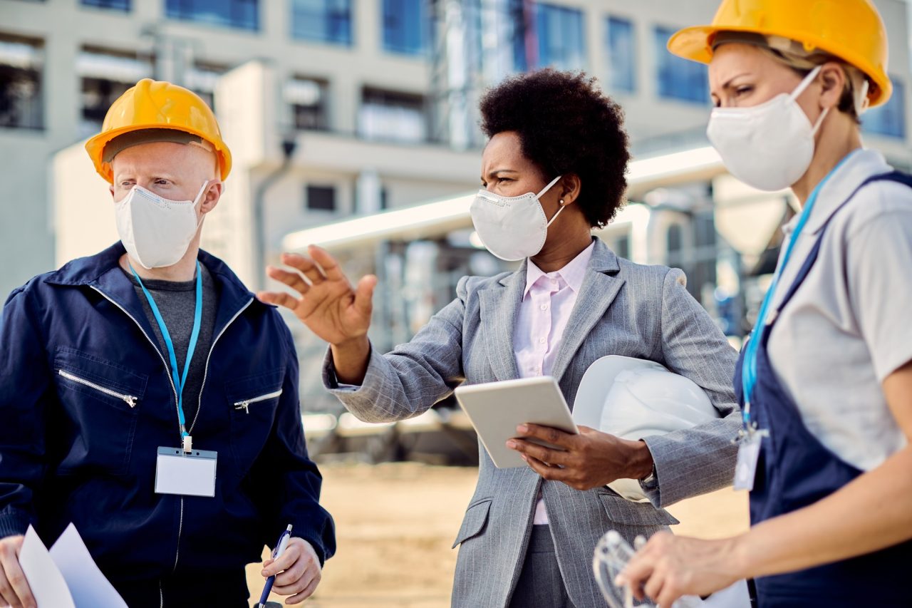 black female architect and civil engineers with protective face masks talking at construction site .jpg